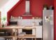 Μικρή κουζίνα σε σοφίτα με κόκκινο τοίχο, ανοιχτή νησίδα αποθήκευσης και λευκά ντουλάπια.